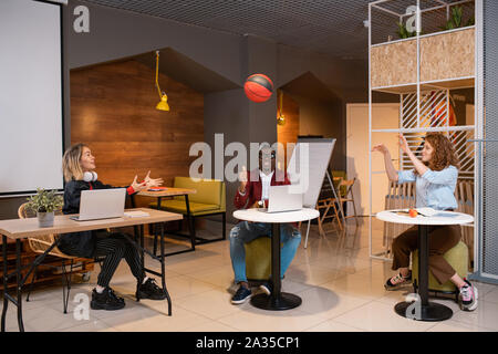 Felice di tre giovani studenti lanciando la palla a ogni altro mentre è seduto in cafe Foto Stock