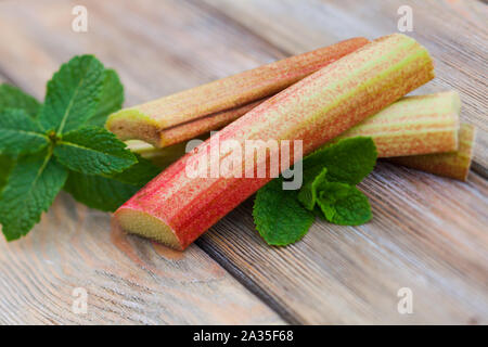 Rabarbaro fresco e foglie di menta su un tavolo di legno Foto Stock