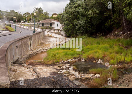 Fiume dalle calde acque sulfuree, tra una strada e una foresta. Edificio in background. Area del famoso centro termale. Furnas, Sao Miguel, isole Azzorre, Foto Stock