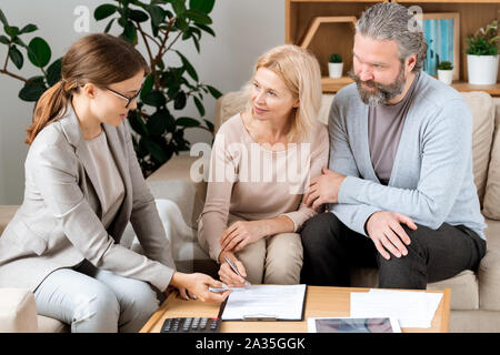 Coppia donna bionda ascolto di agente immobiliare mentre andando a firmare il contratto Foto Stock