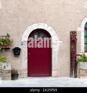 Una vista in dettaglio di una vecchia casa in pietra davanti in Belgio con una porta rossa e la vecchia pompa acqua accanto a letti di fiori Foto Stock