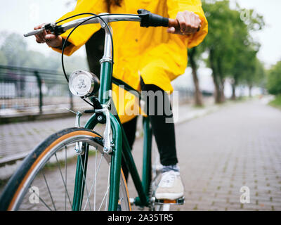 Giro in bicicletta sotto la pioggia. Chiusura del ciclista indossando un impermeabile giallo Foto Stock