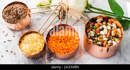 Rame tazze di misura sulla tavola di marmo con fagioli e cereali in cucina. O di cottura di alimenti sfusi concetto di acquisto Foto Stock