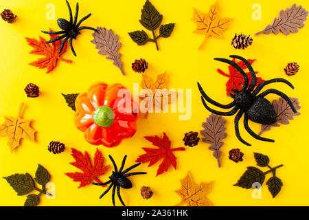 Vista di zucca, foglie di autunno, nero ragni e pigne su sfondo giallo. Concetto di Halloween, laici piatta Foto Stock