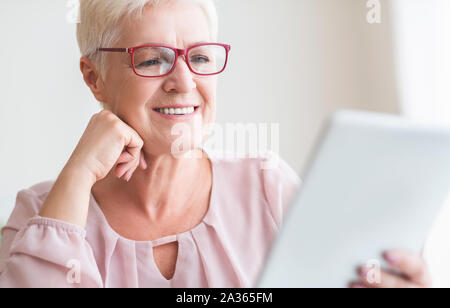 Sorridente bella donna senior libro di lettura sulla tavoletta digitale Foto Stock