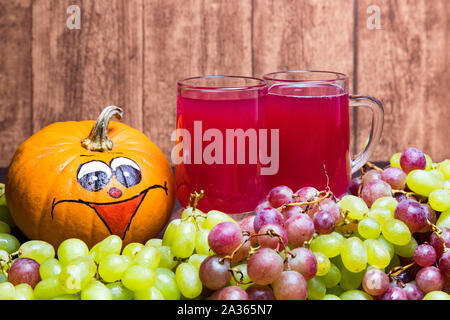 Due bicchieri di rosso stum con un po' di verde e di uve rosse e una divertente zucca fotografato di fronte ad una parete in legno. Foto Stock