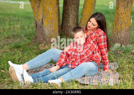 Madre e figlio, disteso sul copriletto, figlio acciglia, portamonete le sue labbra e guarda al lato. Foto Stock