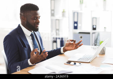 African American businessman meditando in office, rilassante durante la lavorazione Foto Stock