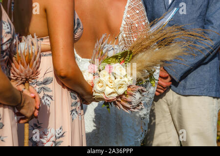 Bridesmaids azienda fiori e bouquet, sposa e lo sposo in piedi nel corso di una cerimonia di matrimonio. Nessun volto. Foto Stock