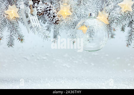 Inverno sfondo innevato con abete del ramo decorato con sfera di vetro, legno slitte, star ghirlande di luci Foto Stock