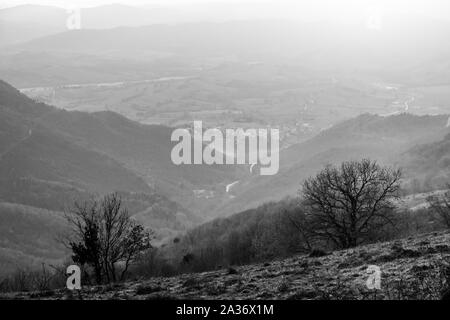 Moody tramonto sul Monte Cucco (Umbria, Italia), con albero in primo piano e il sole che filtra attraverso le nubi Foto Stock