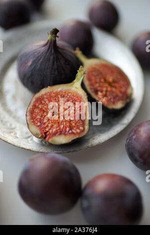 Mature violetta fichi, tagliate a metà e tutto in argento vintage piastra e su un tavolo bianco intorno a. Arte selettiva di messa a fuoco. Foto Stock