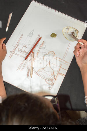 La donna a fumare marijuana giunto durante una pausa dopo il disegno. Sfondo con la cannabis bud, schizzo e shell posacenere. Concetto di droga nell'arte. Foto Stock