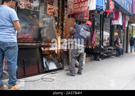 Una strutturale del ferro & acciaio lavoratore lavora su una vetrina porta mentre un collega scherma il negozio adiacente da scintille. In Jackson Heights, Queens, NYC. Foto Stock