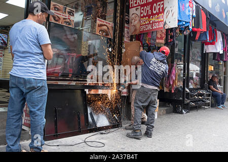 Una strutturale del ferro & acciaio lavoratore lavora su una vetrina porta mentre un collega scherma il negozio adiacente da scintille. In Jackson Heights, Queens, NYC. Foto Stock