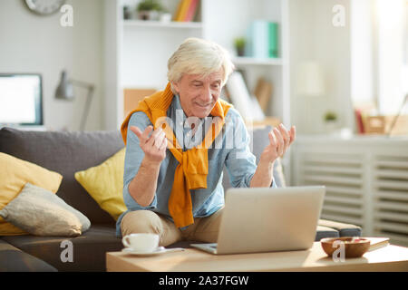 Ritratto di senior emozionale uomo utilizzando laptop seduto sul divano di casa e la visione di gioco di sport o di news, spazio di copia Foto Stock