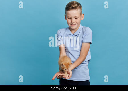 Happy little boy tenendo un gatto sul suo palms, ragazzo adora cat , guardando con tenera espressione, close up ritratto, isolato sfondo blu Foto Stock