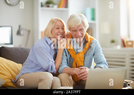 Ritratto di felice coppia senior utilizzando laptop a casa, sia guardando lo schermo e sorridente, spazio di copia Foto Stock