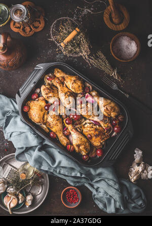 Arrosto di cosce di pollo Cosce di pollo disossate con cipolla rossa e uva in ghisa casseruola padella in scuro dello sfondo rustico con utensili da cucina erbe e spazi, Foto Stock