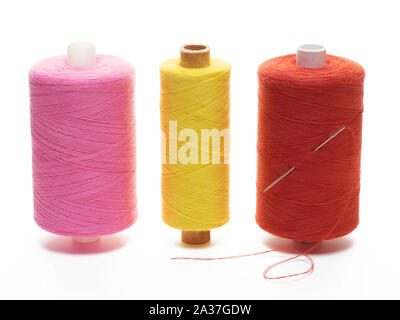 Tre bobine, giallo, rosso e rosa thread in posizione verticale con un ago su sfondo bianco Foto Stock