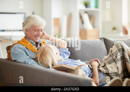 Ritratto di felice coppia senior godendo il tempo libero insieme sdraiati su un comodo divano a casa, spazio di copia Foto Stock