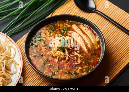 Pollo zuppa Manchow nel vaso nero in ardesia scuro dello sfondo. Pollo zuppa Manchow è indo-cinese piatto di cucina con peperoni, verze, carote, nu Foto Stock