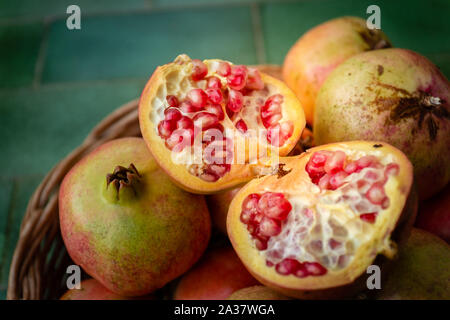 Close-up di un melograno aperto in un cesto pieno di melograni. Frutta fresca dalla regione Puglia, Italia Foto Stock