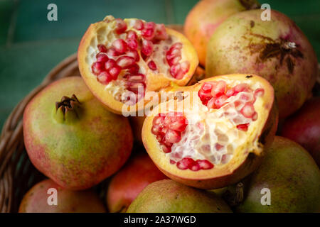 Close-up di un melograno aperto in un cesto pieno di melograni. Frutta fresca dalla regione Puglia, Italia Foto Stock