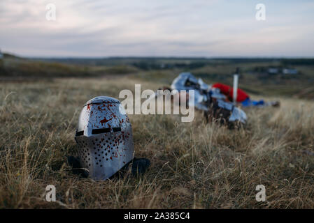 Casco in sangue, cavaliere morto sullo sfondo Foto Stock