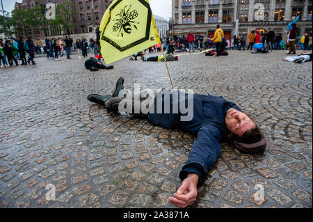 Un attivista del clima getta a terra mentre si tiene un flag durante le prestazioni.Prima della estinzione internazionale ribellione settimana inizia a Amsterdam, un gruppo di attivisti XR riuniti nel centro della città per fare un popolo con la dichiarazione di crisi climatica. Essi hanno anche eseguito un 'die-in-action", che coinvolge un gruppo di persone il montaggio in un luogo e far cadere morto a terra mentre vestito tematicamente e mantenendo una adeguata di poster e insegne. Foto Stock
