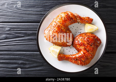 Tradizionale appiccicosa vetrate di cosce di pollo servito con il limone closeup su una piastra sul tavolo. Parte superiore orizzontale vista da sopra Foto Stock