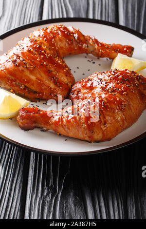 Porzione di pollo sticky trimestre gambe con semi di sesamo e limone close-up su una piastra verticale. Foto Stock