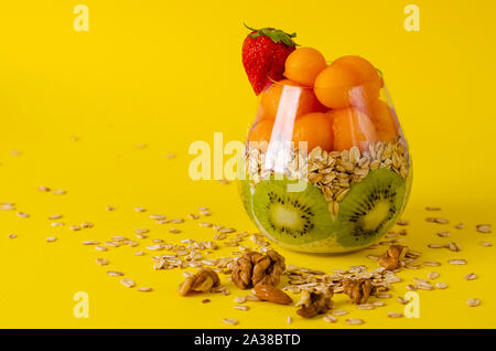 Budino di Chia con kiwi, oatmeals e melone o papaia le palline in un vetro luminoso su sfondo giallo. Detox e sana colazione superfoods concep Foto Stock