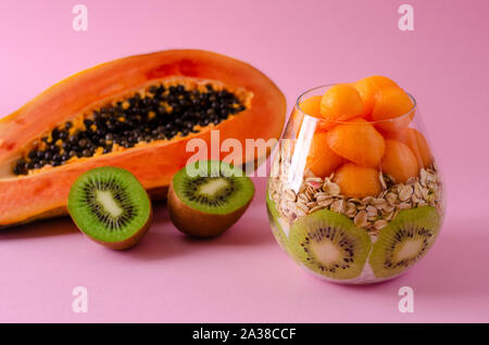 Fresche kiwi, papaia e oatmeals per una sana prima colazione su sfondo viola. La dieta del mangiare e del concetto di nutrizione. Copia spazio, vista frontale Foto Stock