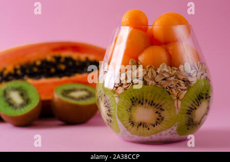 Fresche kiwi, papaia e oatmeals per una sana prima colazione su sfondo viola. La dieta del mangiare e del concetto di nutrizione. Copia spazio, vista frontale Foto Stock