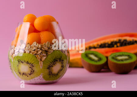 Budino di Chia con kiwi, oatmeals e papaia le palline in un vetro su sfondo viola. Detox dieta e colazione superfoods concetto. Spazio di copia Foto Stock