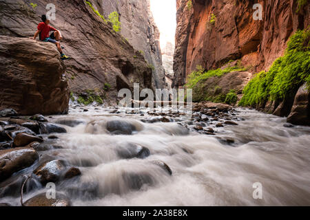 Escursionista seduto su un masso nello Slot Canyon, la si restringe, Parco Nazionale Zion, Utah, Stati Uniti Foto Stock