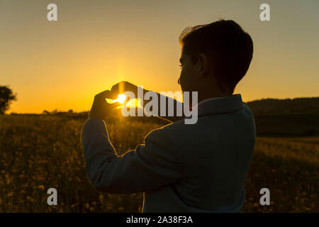 Ragazzo che a forma di cuore con le sue mani al tramonto, Spagna Foto Stock