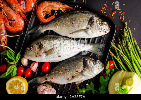 Dorado fresco pesce e gamberi tigre sul ferro padella per grigliare e verdure per la cottura. Mediterranean Seafood concetto. Foto Stock