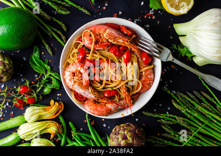 Un piatto di deliziosa pasta italiana con gamberoni o gamberetti e verdure fresche su sfondo nero. Una sana cucina mediterranea concetto. Foto Stock