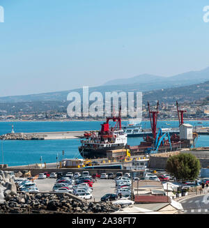 Rethimno, Creta, Grecia. Settembre 2019. Nave da carico a fianco della banchina in questo piccolo porto cretese. Parcheggio auto sul fronte mare. Foto Stock