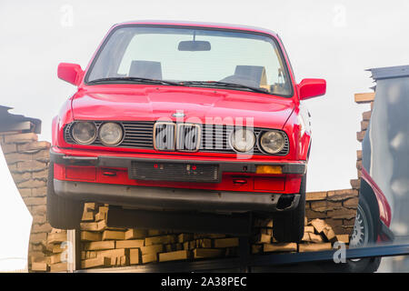 Un rosso BMW auto appeso precariamente dal tetto di un edificio, come se avesse appena spezzato attraverso come il risultato di un incidente, Rotterdam, Paesi Bassi. Foto Stock