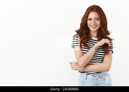 Attraente felice redhead ragazza con le lentiggini in striped t-shirt, braccio trasversale modesto, ridendo gioiosamente, avente divertente conversazione, sorridente e adorazione Foto Stock