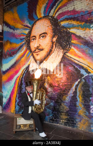 Krysztof Werkowicz è un musicista di strada internazionale sensazione dalla Polonia che riproduce un custom-made tuba che belches fiamme fuori la parte superiore. Nella foto qui suonava in il Clink Street Tunnel, Bankside, Londra, Regno Unito. Dietro Krysztof è il William Shakespeare murale dipinto da Australian artista di strada Jimmy C. fiamme dalla tuba illuminato testa di Shakespeare. Foto Stock