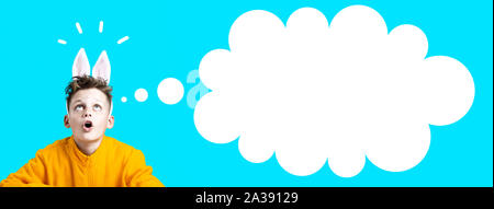 Ragazzo sorpreso in una giacca gialla e le orecchie di lepre su uno sfondo blu Foto Stock