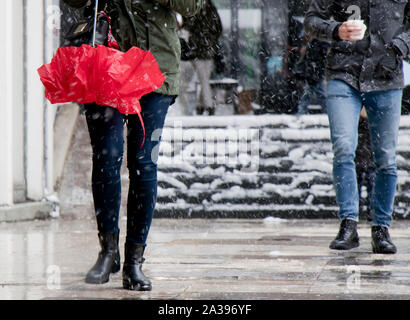 I giovani a camminare sulla neve winter city marciapiede, tenendo ombrellone e bevanda calda, dalla vita in giù Foto Stock