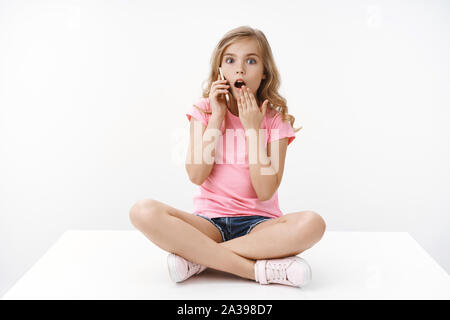 Scioccato affascinante giovane ragazza blong bambino parlando al telefono, tenere lo smartphone a soffocare, aprire bocca lo sguardo attonito fotocamera sorpreso sentire incredibile gossip Foto Stock