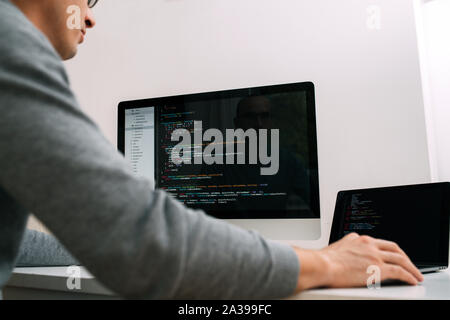 Programmatore, lavorando dietro la scrivania, analizzando il codice sullo schermo nero. Foto Stock