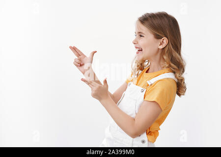 Gioiosa carino bambina divertirsi giocando con gli amici, puntare il dito pistole, cercando fare bang-bang segno lasciato a sorridere e ridere allegramente Foto Stock