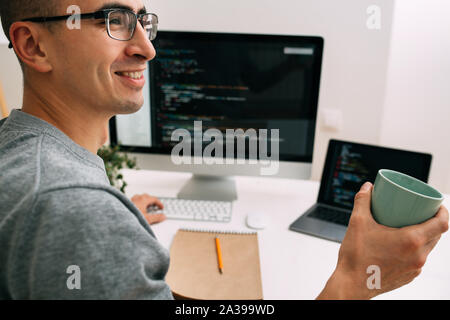 Programmatore, lavorando dietro la scrivania con due schermi riempito con linee di codice Foto Stock